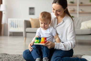 Bir anne, genç oğluyla yerde oturup canlı yapı taşlarıyla oynar. Doğal ışıkla dolu parlak ve rahat oturma odalarında nişanlı ve mutlular..