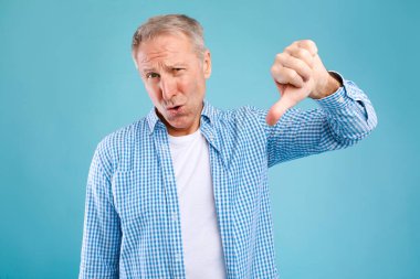 Olgun bir adam mavi bir arka plana karşı durur, kaşlarını çatar ve baş parmak işareti yapar. Vücut dili açıkça hayal kırıklığını ve hoşnutsuzluğu yansıtıyor, duygularını vurguluyor..