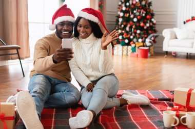 Noel Baba şapkası takan neşeli siyah bir çift yerde bir battaniyenin üzerinde oturuyor, arkadaşlarını veya ailelerini aramak için cep telefonu kullanıyorlar. Noel 'i kutlamak için ellerini sallıyorlar..