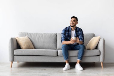 Neşeli bir Arap adam oturma odasında rahat bir kanepeye oturur ve kahvesini yudumlar. Boş haftasonunda bir anlık rahatlamayı, hayal kurmayı ve gevşemeyi sever..