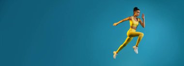 Atletik bir dişi, odaklanmış bir ifadeyle koşarken havada yakalanır. Parlak bir kıyafet giyiyor ve enerjik bir şekilde poz veriyor. Mavi bir arkaplan karşısında hareket hissi yaratıyor..