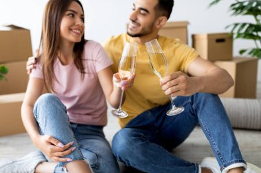 İki neşeli insan yerde oturup, yeni evlerinde şampanya kadehleriyle kadeh kaldırarak gülümsüyor. Rahat atmosferleri gelecekleri için mutluluk ve heyecanı yansıtıyor..