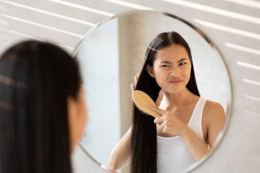 Banyo ortamında, genç bir kadın gür, kıvırcık saçlarını tararken sinirli görünür. Ayna, hasarlı saçlarıyla kavga ederken onun sinirlerini yansıtıyor..