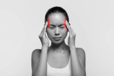 Genç bir Asyalı kadın stüdyoda baş ağrısından dolayı acı çekiyor. Sinirli bir bakışla şakaklarına dokunuyor. Görüntü siyah beyaz ve kafasında kırmızı röfleler var..