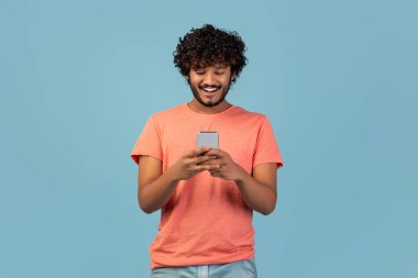 Neşeli bir Hintli cep telefonunu mavi bir stüdyoda kullanıyor. Arkadaşlarıyla sohbet ederken ve oyun oynarken gülümsüyor, dijital dünyaya bağlı olarak geçirdiği zamanın tadını çıkarıyor..