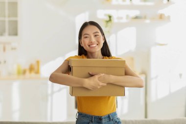 Neşeli Asyalı bir bayan internetten aldığı şeylerle dolu bir karton kutuya sevinçle sarılıyor..