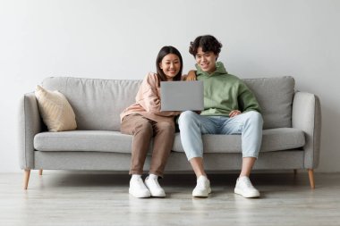 Kanepede kucaklaşan Asyalı sevgili bir çift dizüstü bilgisayarlarında video izliyor. Rahat bir ev ortamında birbirlerine bağlı kalarak, boş zamanlarının tadını çıkarıyorlar..