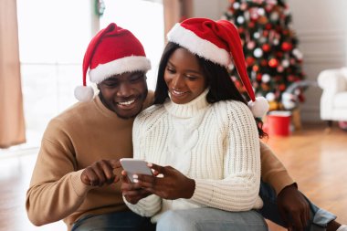 Neşeli şapkalı gülümseyen Afrikalı Amerikalı çift dekore edilmiş bir oturma odasında birlikte oturuyorlar..