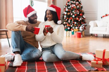 Sevgi dolu siyah bir çift yerde rahat bir battaniyeyle oturur, kırmızı Noel Baba şapkaları giyer ve kahveyi paylaşırlar. Noel arifesini hediyeler ve süslü bir ağaçla kutlarlar..