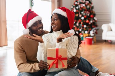 Neşeli siyah bir çift yerde oturuyor, hediyelerini vererek Noel 'i kutluyorlar. Kadın, erkek ona bir hediye verirken heyecanlanıyor. Arkalarında bir Noel ağacı süslenmiş..