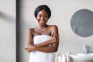 Genç siyah bir bayan beyaz bir havluya sarılmışken kameraya gülümsüyor. Nazikçe tenine dokunuyor, omuzlarını kucaklıyor..