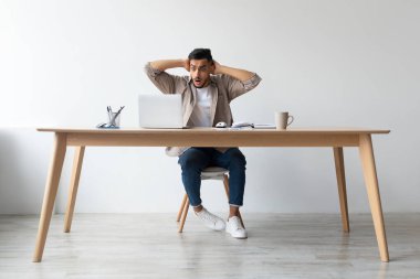 Şok olmuş bir Arap, tahta bir masada dizüstü bilgisayarla oturur ve başı derttedir. Uzaktan çalışırken endişe verici haberlere tepki veriyor. Ofisinde gergin bir an yaşanıyor..