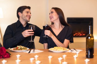 Bir çift mum ışığı ve kırmızı şarapla evde sıcak bir akşam yemeğinin tadını çıkarıyor. Gülücükleri ve kahkahaları paylaşıyorlar, lezzetli yemeklerin tadını çıkarıyorlar ve birbirlerine eşlik ediyorlar..