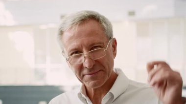 Profesyonel kıyafetli yaşlı bir adam, ofis ortamında iş arkadaşlarıyla etkileşime girer. Kendinden emin ve meşgul görünüyor, dinamik bir iş ortamı yaratıyor..