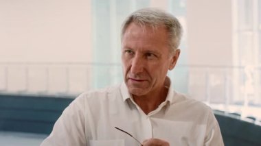 Profesyonel kıyafetli yaşlı bir adam modern bir ofiste işle ilgili görevlere girişiyor. Belgeleri incelerken ifadesi konsantrasyonu gösteriyor. Doğal ışık boşluğu doldurur..