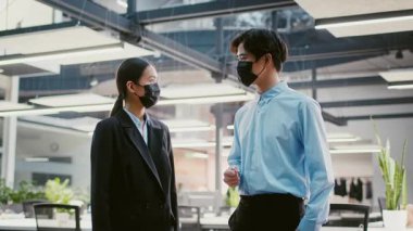 İki genç Asyalı profesyonel parlak ışıklandırma ve yeşillik ile geniş, çağdaş bir ofiste fikirleri tartışıyor. Yoğun bir iş gününde işbirliği ve yeniliğe odaklanırlar..