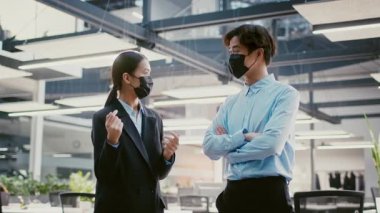 İki genç Asyalı profesyonel çağdaş bir ofiste canlı bir tartışmaya giriştiler. Her ikisi de maske takıyor ve etrafları aydınlık, açık bir çalışma alanıyla çevriliyken hevesli görünüyorlar..