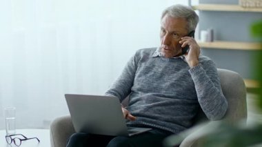 60 'lı yaşlarda yaşlı bir adam rahat bir şekilde koltukta oturur. Ev ve iş odaklı modern bir yaşam tarzını yansıtan dizüstü bilgisayarı kucağında dururken telefonda konuşuyor..