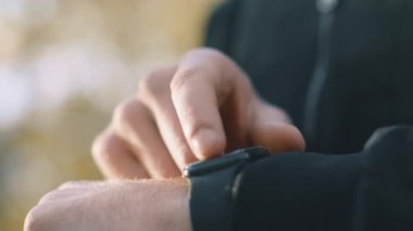 Genç bir adam antrenman sürecini izlemek için yolda koşuyor, spor takip cihazını kontrol ediyor. O, açık hava atmosferinin tadını çıkarırken sağlıklı bir yaşam tarzına sahiptir..