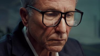 Takım elbiseli ve büyük gözlüklü son sınıf öğrencisi modern bir ofiste çalışıyor. Atmosfer, üretkenlik ve profesyonelliğe odaklı kurumsal bir yaşam tarzını yansıtıyor..