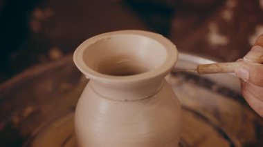 Orta yaşlı bir adam atölyesinde iyi işlenmiş kil çömlekçiliğine odaklanır. Elleri, ıslak çamuru güzel ve eşsiz parçalara ayırmak için ustalıkla çalışıyor. Atmosfer sakin ve yaratıcı..
