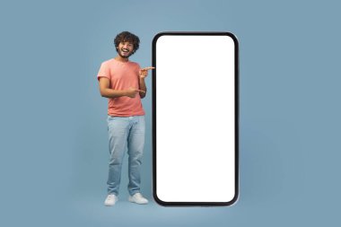 Kıvırcık saçlı neşeli bir doğulu adam boş ekran ile büyük bir akıllı telefonu işaret ederken gülümsüyor. Parlak mavi bir stüdyoda çekici bir mobil teklif sunuyor..