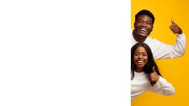 İki mutlu birey yan yana, gülümseyerek başparmak kaldırıyor. Parlak sarı bir arka plana karşı poz veriyorlar, günlük kıyafetlerinde neşe ve pozitiflik sergiliyorlar..