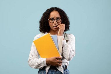 Mavi bir stüdyoda elinde not defterleri ve sırt çantası olan bir kız öğrenci duruyor. Tırnaklarını panik içinde yiyor, yaklaşan üniversite sınavı için çok endişeleniyor. Stres ve endişelerini gösteriyor..