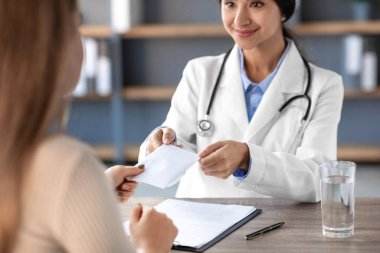 Genç Hintli doktor klinikte mali işlemlerini yaparken gülümsüyor. Ayarlar, potansiyel yolsuzluğa işaret eden profesyonel bir sağlık ortamını yansıtıyor.