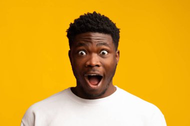 Genç bir adam şaşkınlığını geniş gözleri ve açık ağzıyla gösterir. O, beyaz bir gömlek giyiyor, neşeyle gülümsüyor. Parlak sarı arka plan, o anın coşkusunu arttırır..