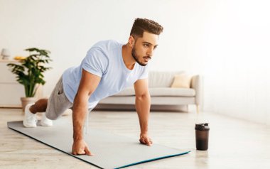 Genç bir adam, parlak ve ferah bir oturma odasında yoga minderinde şınav çekiyor. Bir kahve fincanı yakınlarda oturuyor, sabah egzersizlerinin altını çiziyor..