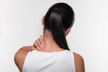 Uzun saçlı bir kadının boynunu ovması ofis sendromundan rahatsızlık belirtileri gösteriyor. Beyaz stüdyo arka planı onun acı ve gerilimle mücadelesini vurguluyor..