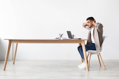 Stresli bir Arap, basit bir odada masa başında oturur ve dizüstü bilgisayar ekranına bakarken kafasını tutar. Gün boyunca olumsuz iş haberleri yüzünden endişeli gibi görünüyor..