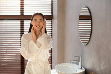 Parlak ve neşeli genç bir kadın şık bir banyoda düzgün yüzüne dokunurken kameraya gülümsüyor. Tazelenmiş teninin tadını çıkarıyor. Sabah rutininden sonra..