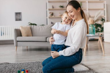 A mother and her young son share a joyful moment in their comfortable living room. They smile at each other while playing, creating a warm family atmosphere.