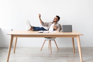 Orta Doğulu bir adam sandalyeye yaslanıyor ve sanal gitar çalıyor. Ofis masasında işe ara verirken kablosuz bir kulaklık takıyor ve gülümsüyor..