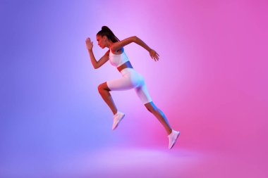 Sportif bir kadın, egzersiz yaparken azmini gösterirken havada yakalanır. Kardiyo egzersizi sırasında çarpıcı pembe ve mavi bir arka plana karşı beyaz spor giyer..