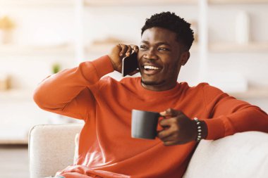 Neşeli bir adam bir koltukta oturuyor, bir elinde bir fincan kahve tutuyor ve diğer eliyle telefonda konuşuyor. O kalın bir kazak giymişti ve oda davetkar hissediyordu..