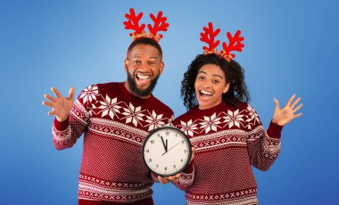 Yeni yıla beş dakika kaldı. Gece yarısına beş dakika kala saati olan neşeli siyah çift geyik boynuzları takıyor ve mavi arka planda kameraya gülümsüyor.