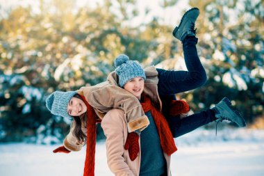 Karlı bir ortamda iki kardeş neşeli bir anı paylaşıyor. Bir çocuk diğerinin sırtında taşınıyor, ikisi de sırıtarak sırıtıyor, karla kaplı ağaçlarla çevrili palto ve şapkalar giyip sıcacık sırıtıyorlar..