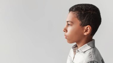 Gri bir arkaplana karşı poz veren ciddi bir siyahi çocuğun profil fotoğrafı. O düşünceli bir ifadeyle yan tarafa bakıyor. Metin veya başlıklar için mükemmel ayar.