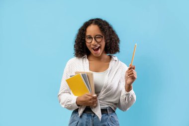 Genç kız öğrenci elinde defterlerle mavi bir arkaplanda gülümsüyor. Heyecan ve ilhamı göstermek için bir kalemi yukarı kaldırır ve harika fikrini paylaşmaya hazırdır..