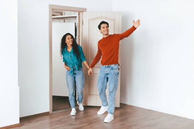 Genç bir çift yeni bir evin girişinde el ele tutuşup gülümsüyor. Yeni maceralarına başlamak için heyecanlı ve hazır görünüyorlar. Parlak, mobilyasız bir yerde..