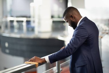 Stresli Afro-Amerikalı takım elbiseli genç girişimci başını öne eğerek ayakta duruyor, iş yerinde zorluklar yaşıyor, arka plan çekimi, fotokopi alanı, finansal kriz ve iş dünyası ile panorama