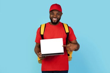Food Delivery Website. Smiling black male courier holding laptop with blank screen, african american deliveryman in uniform showing computer with white monitor, standing on blue background, mockup