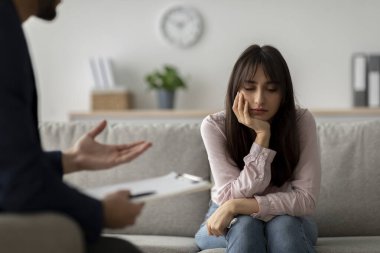 Genç bir Arap kadın doktor muayenehanesinde oturuyor ve psikoloğunu dinlerken mutsuz görünüyor. Dekor, zor zamanlarda psikolojik desteğin önemini vurguluyor..