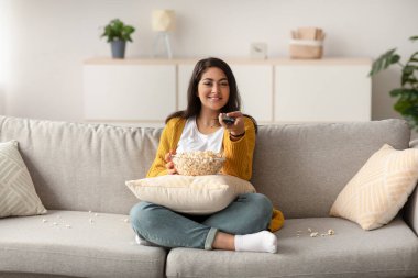 Neşeli bir Arap kadın elinde uzaktan kumanda ve bir kase patlamış mısırla kanepede uzanıyor. Oturma odasında televizyon izlerken rahatlıyor, film gecesi için heyecanlanıyor..