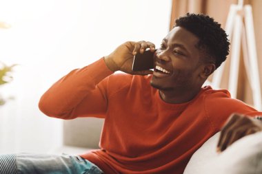 Parlak turuncu kazaklı bir adam büyük bir gülümsemeyle akıllı telefonuyla konuşur. Yumuşak mobilyalar ve bitkilerle çevrili aydınlık bir oturma odasında rahatça oturur ve sohbetinin tadını çıkarır..