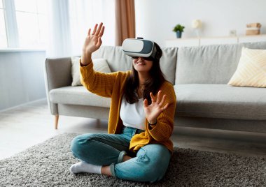 Rahat bir yaşam alanında, genç bir ortadoğulu kadın interaktif bir video oyununa dalmış, sanal gerçeklik gözlüğü takıyor..