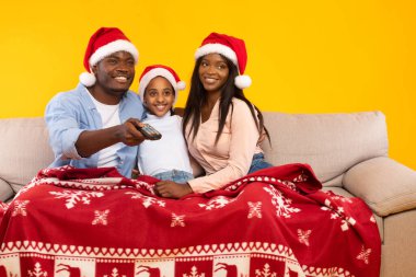 Neşeli bir Afrikalı Amerikalı aile, kırmızı bir battaniyeyle kaplı, rahat bir koltukta oturuyor..